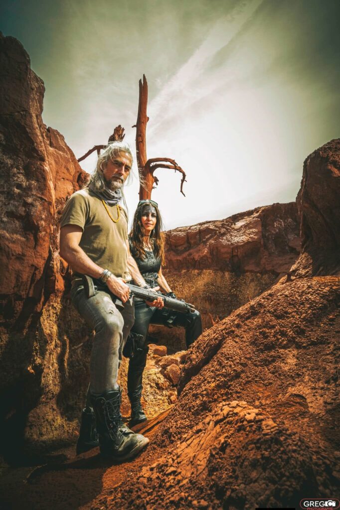 Thalie Némésis vétue de cuir noir et Dard tenant un fusil mitrailleur dans un décor de rochers rouges - Photo © Gregory Collignon