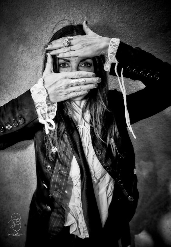 Thalie Némésis vétue de noir et d'un corsage blanc devant un mur délabré - Photo © Dany Rousseau